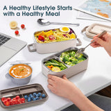 Lifestyle shot of a healthy meal being enjoyed from the cream white stainless steel lunch box on an office desk, featuring fresh vegetables and soup.