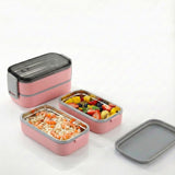 Pink stackable stainless steel bento lunch box opened, displaying meal prep with noodles and fresh fruit.