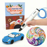 A child's hand holding a white 3D printing pen, creating a blue wireframe toy car with blue filament. The scene includes a "3D PRINTING PEN PICTURE ALBUM" book in the background and a coil of 40-color multi-colored filaments in the foreground.